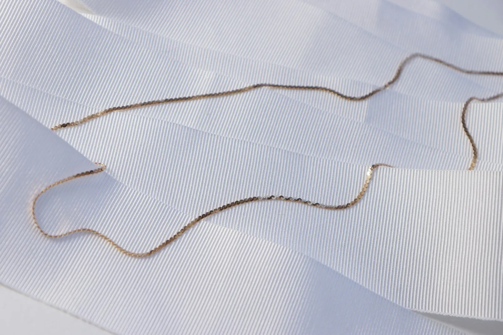 A fine gold chain laid across a wrist, permanent jewelry with no clasp
